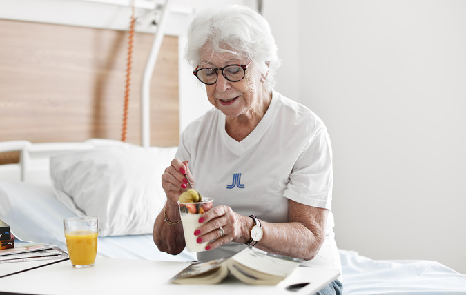 En patient på sjukhus äter en yoghurt med bär som mellanmål.