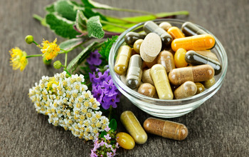 En skål med piller och tabletter av kosttillskott och naturmedicin, bredvid ligger lite örter och blad
