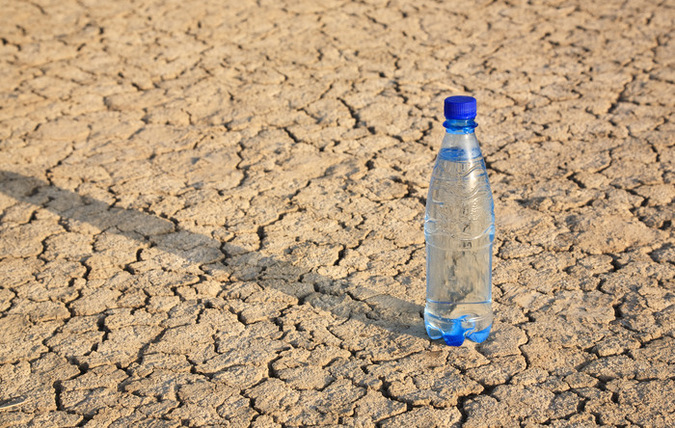 En petflaska med vatten står på en torkad jordyta med sprickor