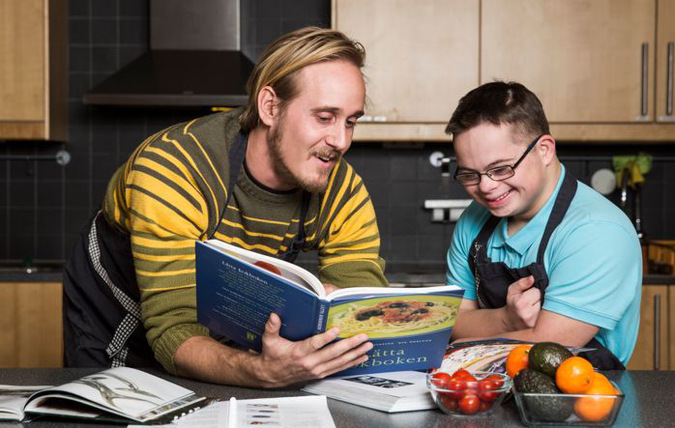 Ett barn och en vuxen står tillsammans i ett kök och tittar i en kokbok.