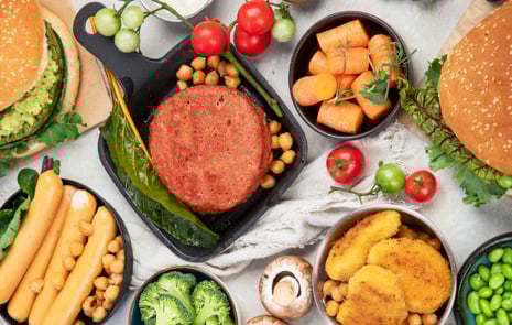 Vegetariska hamburgare, korvar och nuggets, färska grönsaker och såser på vit bakgrund. 