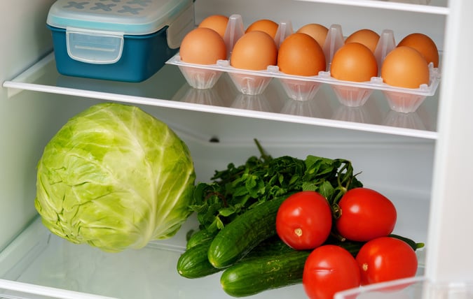Välfyllt kylskåp med fräscha grönsaker och ägg
