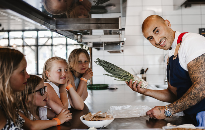 Kock visar matlagning för en grupp barn i sitt kök. Han tittar in i kameran.