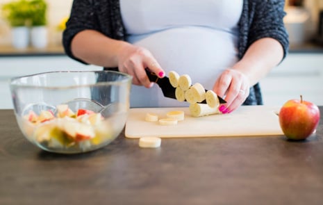 A pregnant woman slicing fruit.