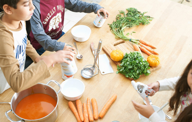 Barn lagar mat vid en köksbänk. På bänken ligger det köksredskap och olika grönsaker.