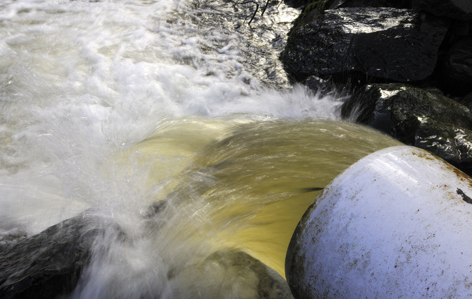 Vatten forsar ut från en stort rör till en vattensamling med stenar vid kanten