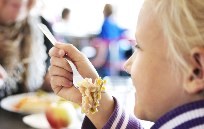 En elev äter skollunch tillsammans med en lärare i en skolrestaurang.