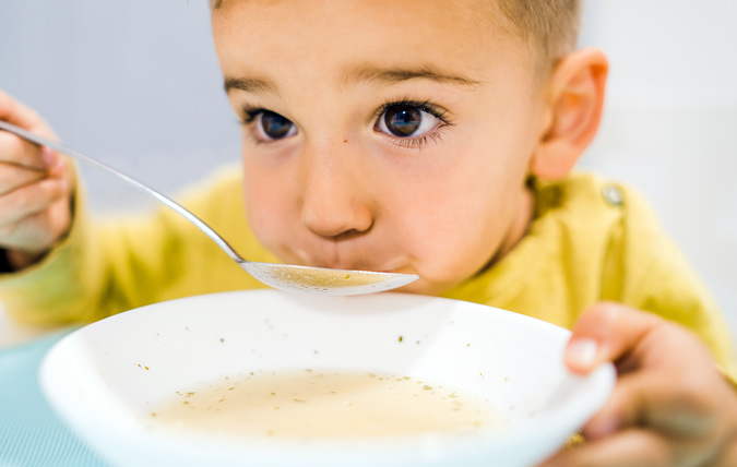 Liten pojke äter soppa med en sked