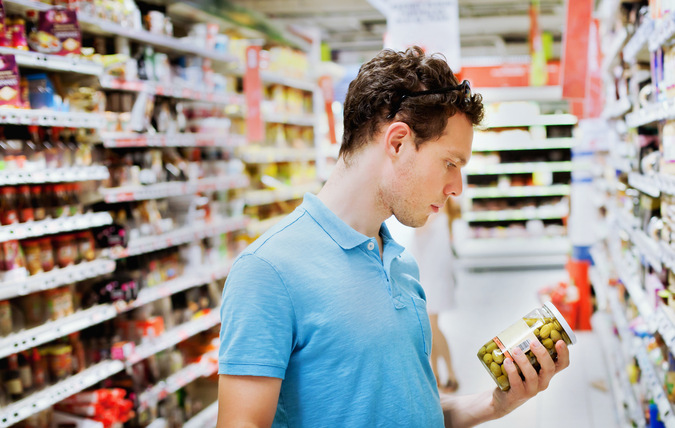 En man som står i en livsmedelsbutik och tittar på en förpackning med oliver