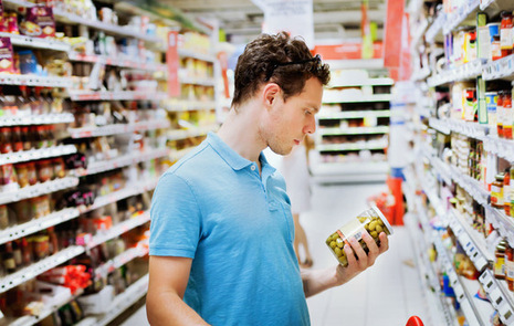 En man som står i en livsmedelsbutik och tittar på en förpackning med oliver