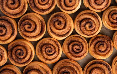 Nybakade kanelbullar, som fyller hela bilden, på bakpapper sett uppifrån .