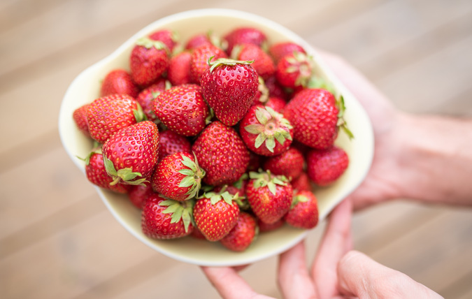 Ett par händer som bär på en skål med orensade jordgubbar