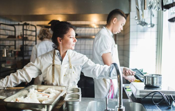 Kock i restaurangkök med vattenkran i förgrunden.