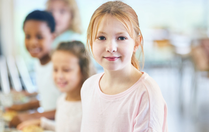 Ett skolbarn som står längst fram i matkön ler och tittar in i kameran
