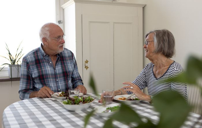 Två äldre personer äter mat i ett kök.