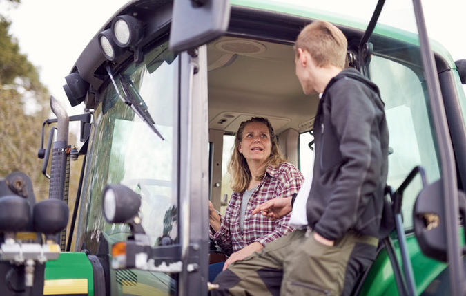 Ung man pratar med bonde i hennes traktor.
