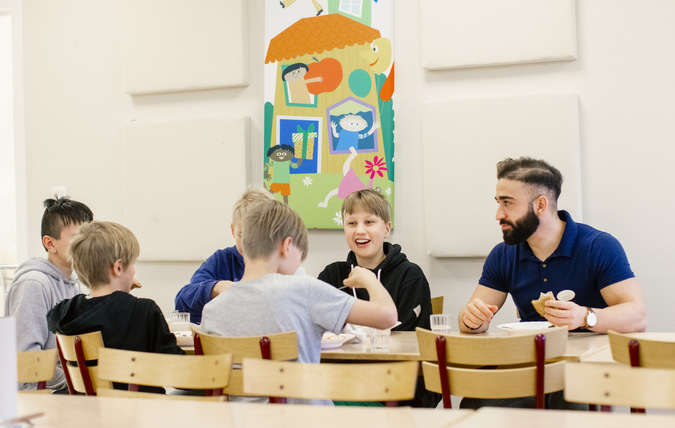 En grupp elever äter tillsammans med en lärare i en matsal.