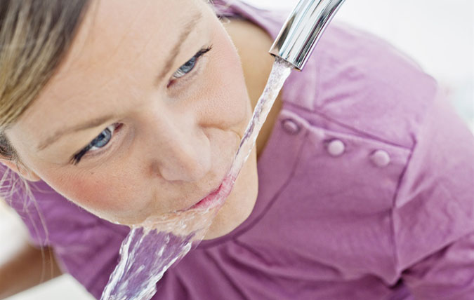Kvinna dricker vatten från en kran.