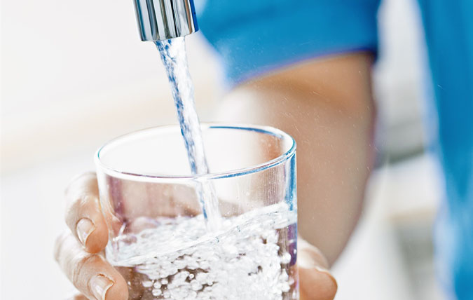 Vatten från kran rinner ner i ett dricksglas